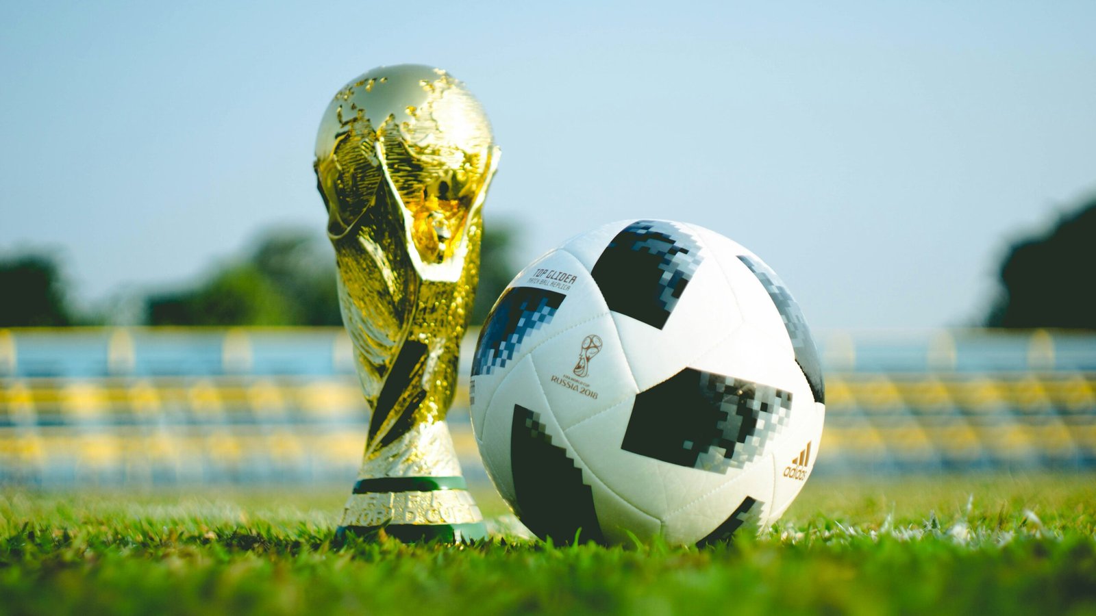 The World Cup trophy next to a match ball on the pitch