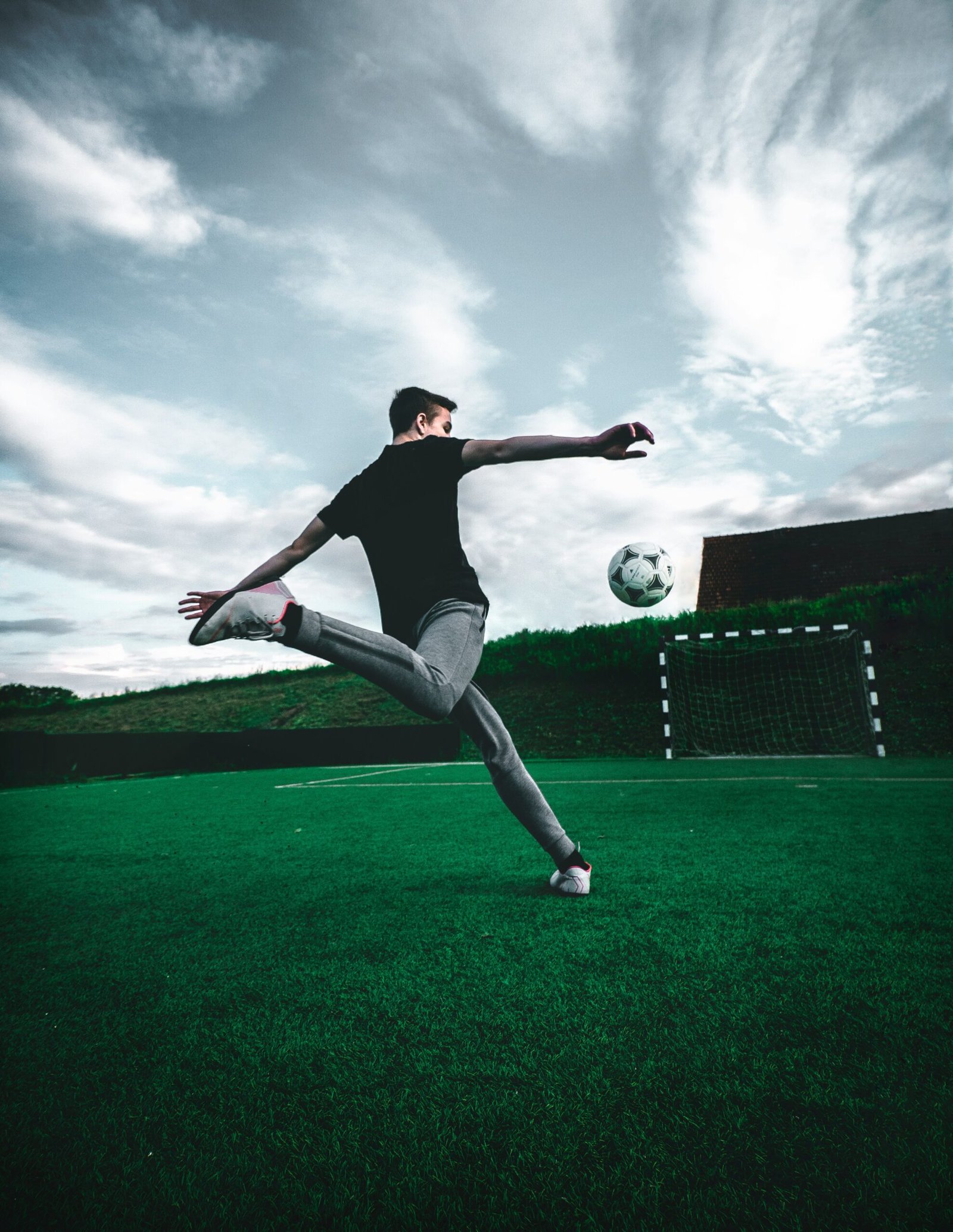 Footballer striking the ball mid-air on an outdoor pitch